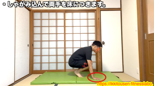 バービージャンプの開始姿勢として、しゃがみ込んで両手を床につける男性